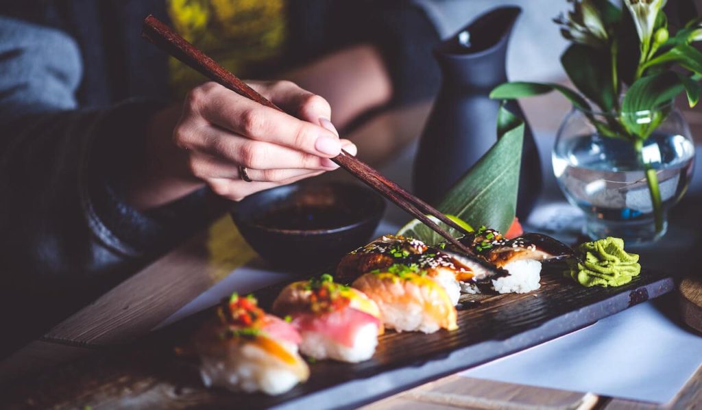 Close up of a lady picking up nigiri sushi with chopsticks